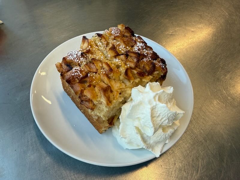 frisch gebackener Apfelkuchen mit Sahne auf wei&szlig;em Porzellanteller in der Hofk&uuml;che von Gut Tangstedt
