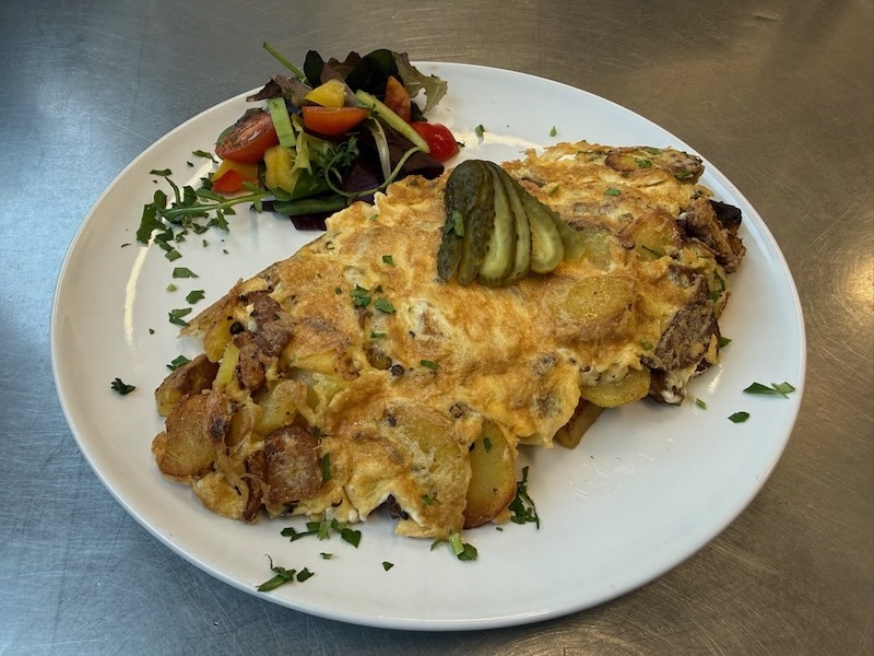 Herzhaftes Bauernfr&uuml;hst&uuml;ck mit goldbraunen Bratkartoffeln und Ei, garniert mit Gew&uuml;rzgurken und serviert mit einem frischen Beilagensalat auf einem wei&szlig;en Teller.